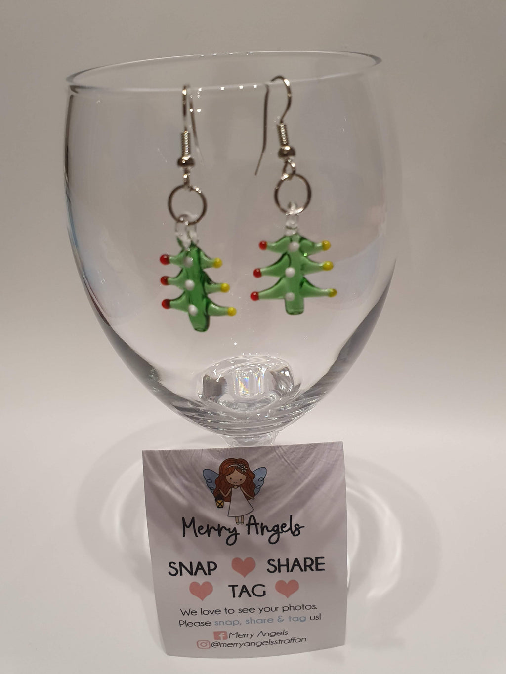 This is a picture of a pair of Christmas tree earrings hanging over a wine glass
