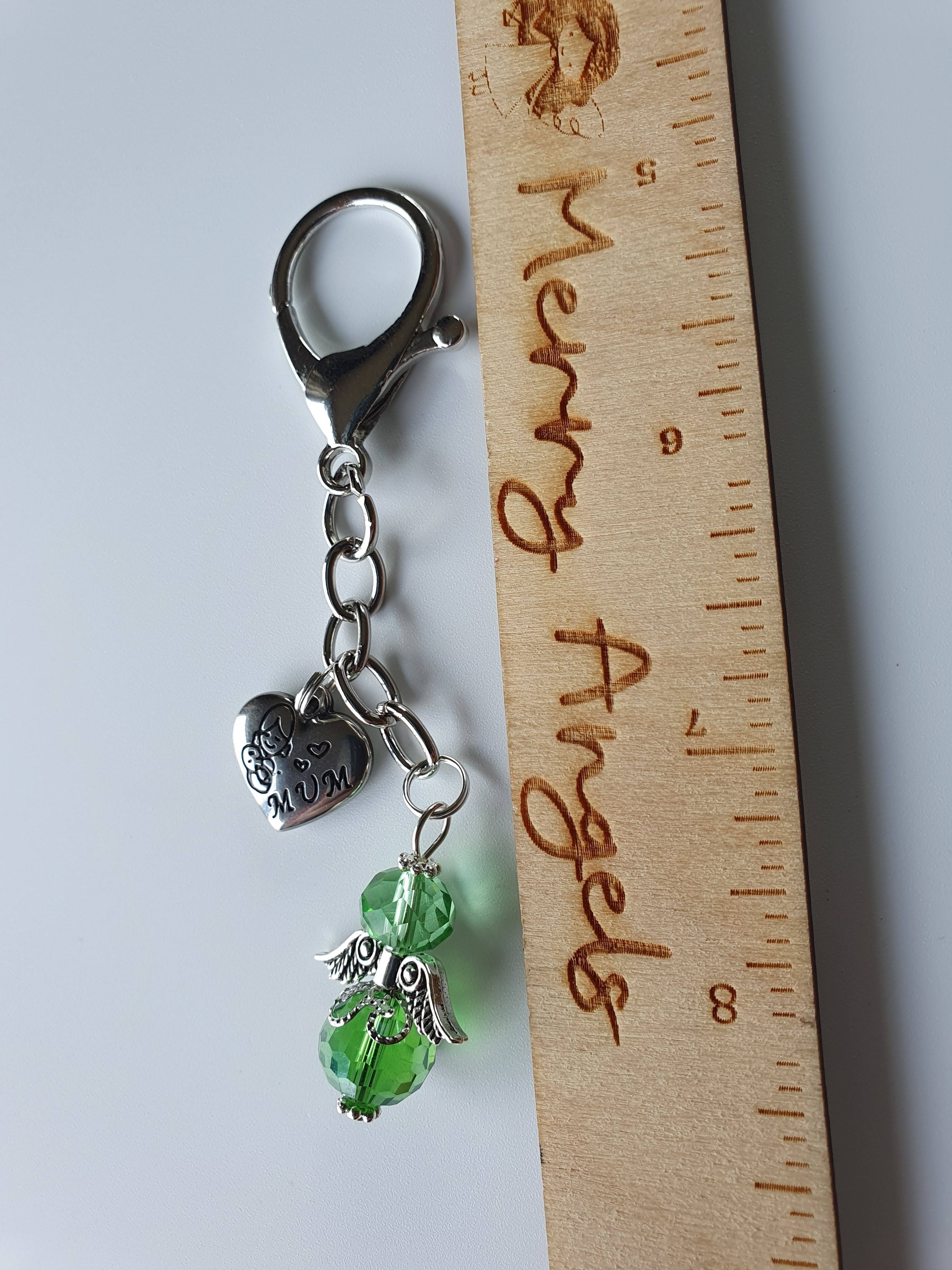 This is a picture of a silver angel keyring with a silver heart charm attached. The charm has the word 'mum' engraved in it. The angel is green. 