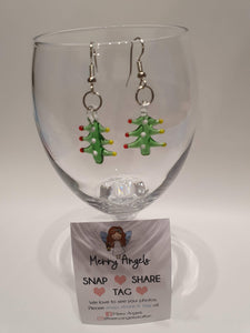 This is a picture of a pair of Christmas tree earrings hanging over a wine glass
