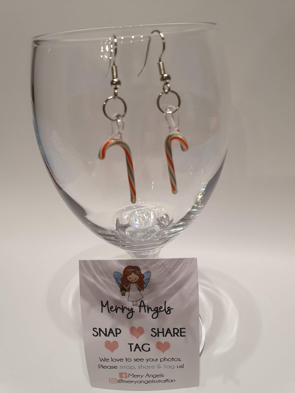 This is a picture of a pair of candy cane earrings hanging over a wine glass 