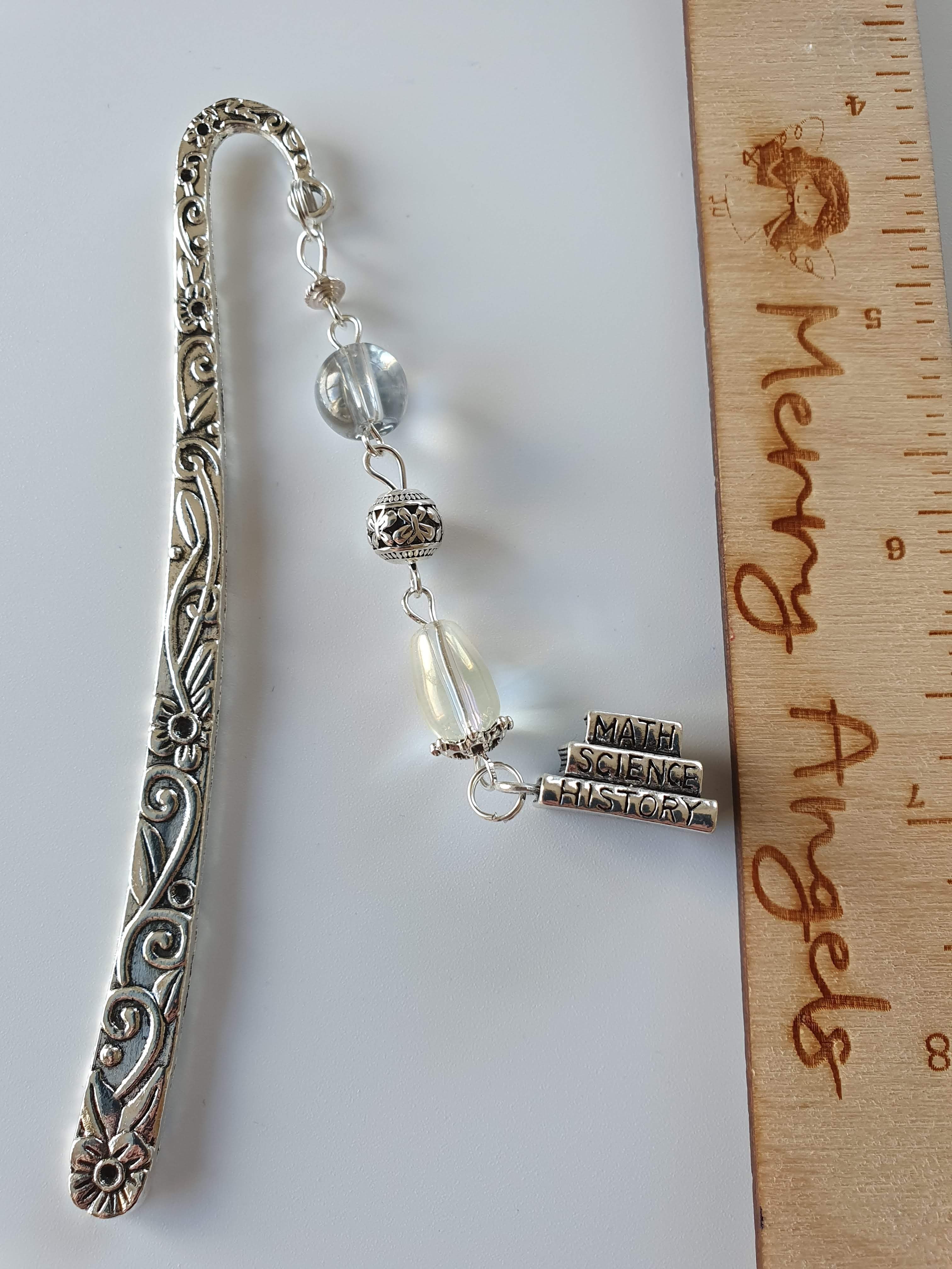 A silver bookmark with a clear and white bead and a book stack charm. 