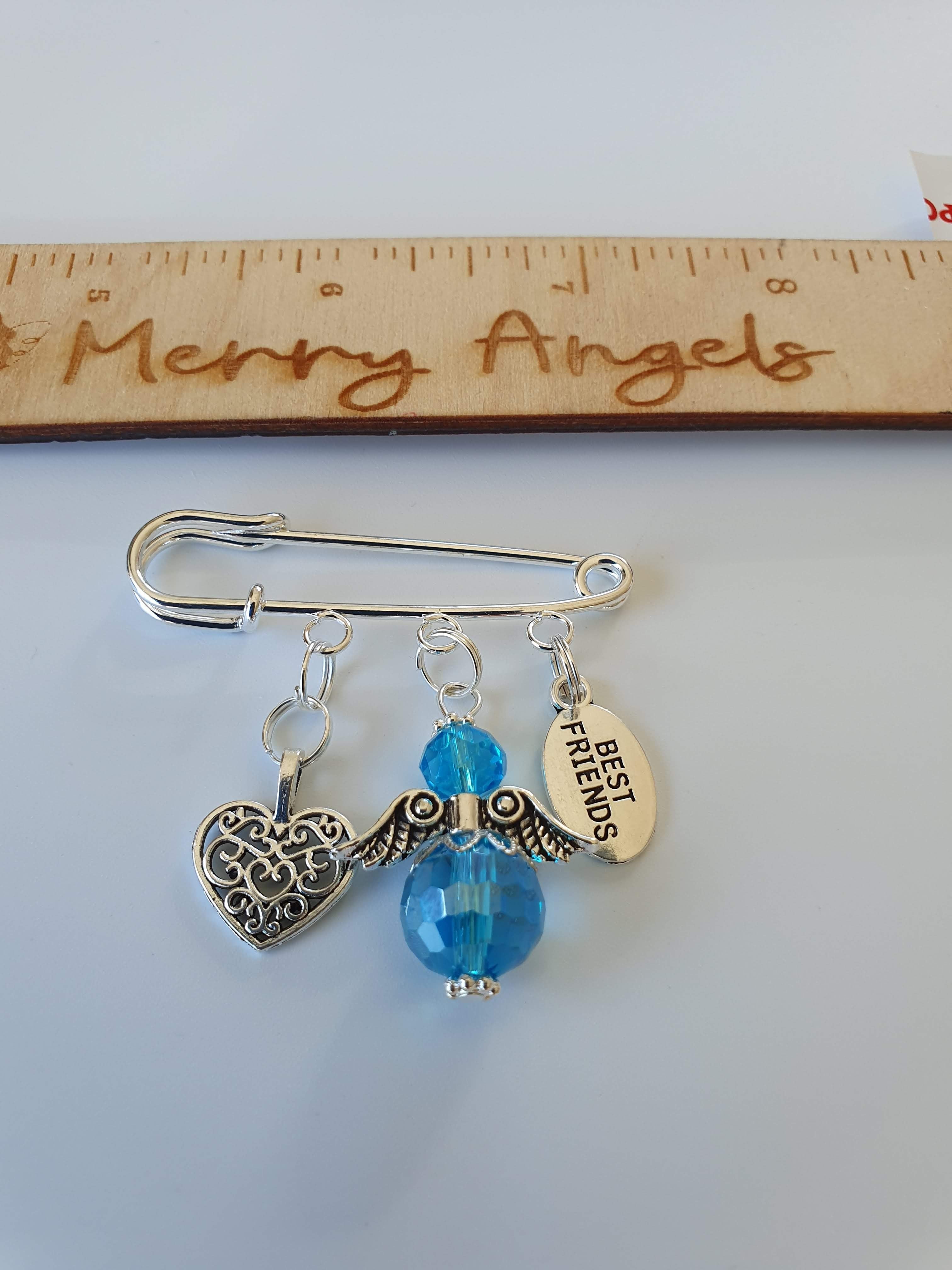 Picture of a silver plated pram pin with a silver heart charm, a blue angel, and a silver 'best friends' charm. 