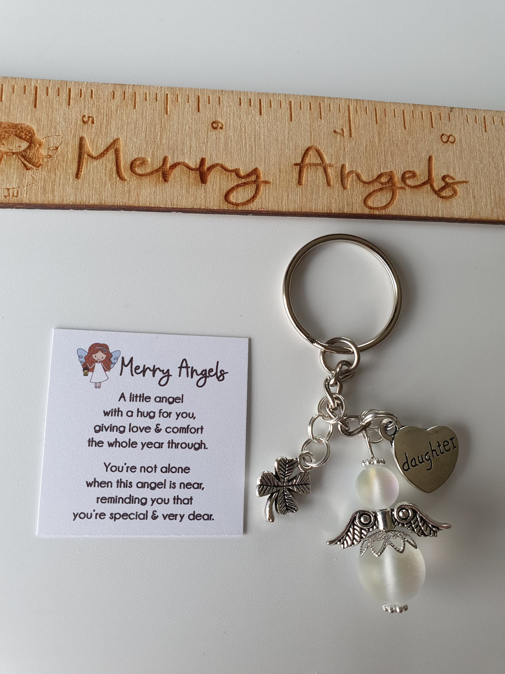 This is a picture of an angel keyring with two silver charms. The charms are a shamrock and a heart with the word 'daughter' engraved in it. 