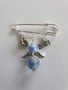 A silver plated pram pin with silver feet charm, a blue angel with silver wings, and a silver 2021 charm. 