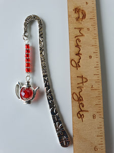 A silver bookmark with red beads and a red teapot hanging from the end. 