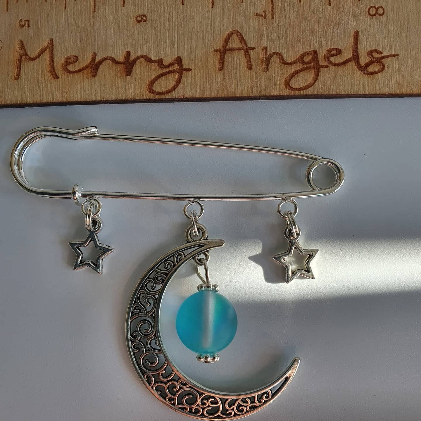 A silver plated pram pin with 2 silver star charms and a silver moon charm with a blue bead hanging from it. 