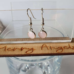 This is a picture of a pair of baby pink earrings hanging over a glass and ruler