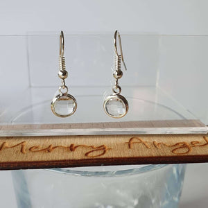 This is a picture of a pair of clear earrings hanging over the side of a wine glass
