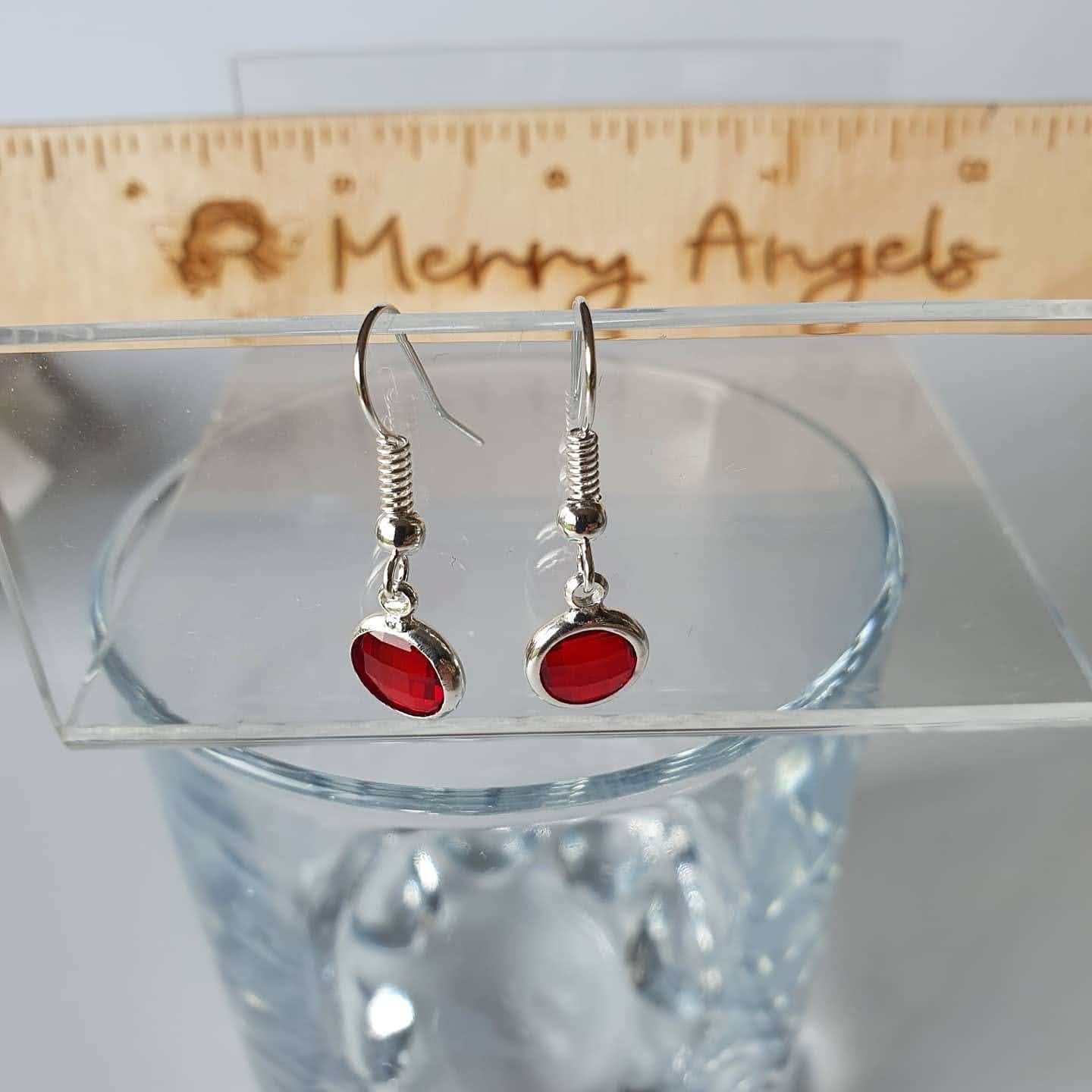 This is a picture of a pair of red earrings hanging over a wine glass