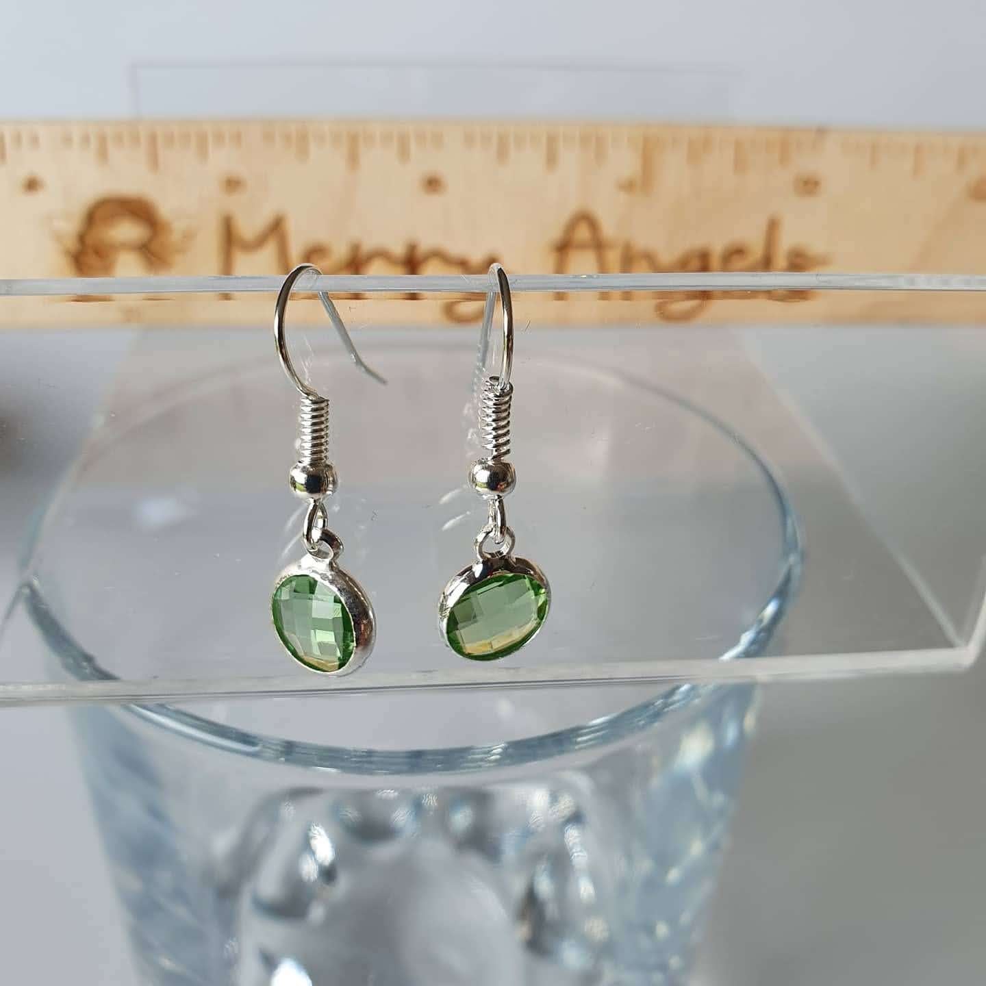 This is a picture of a pair of green earrings hanging over a wine glass