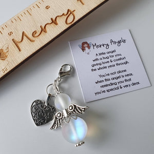 This is a picture of a clear angel hug with silver wings and feet and a silver heart charm attached. There is also a poem about angels printed on a piece of card. 