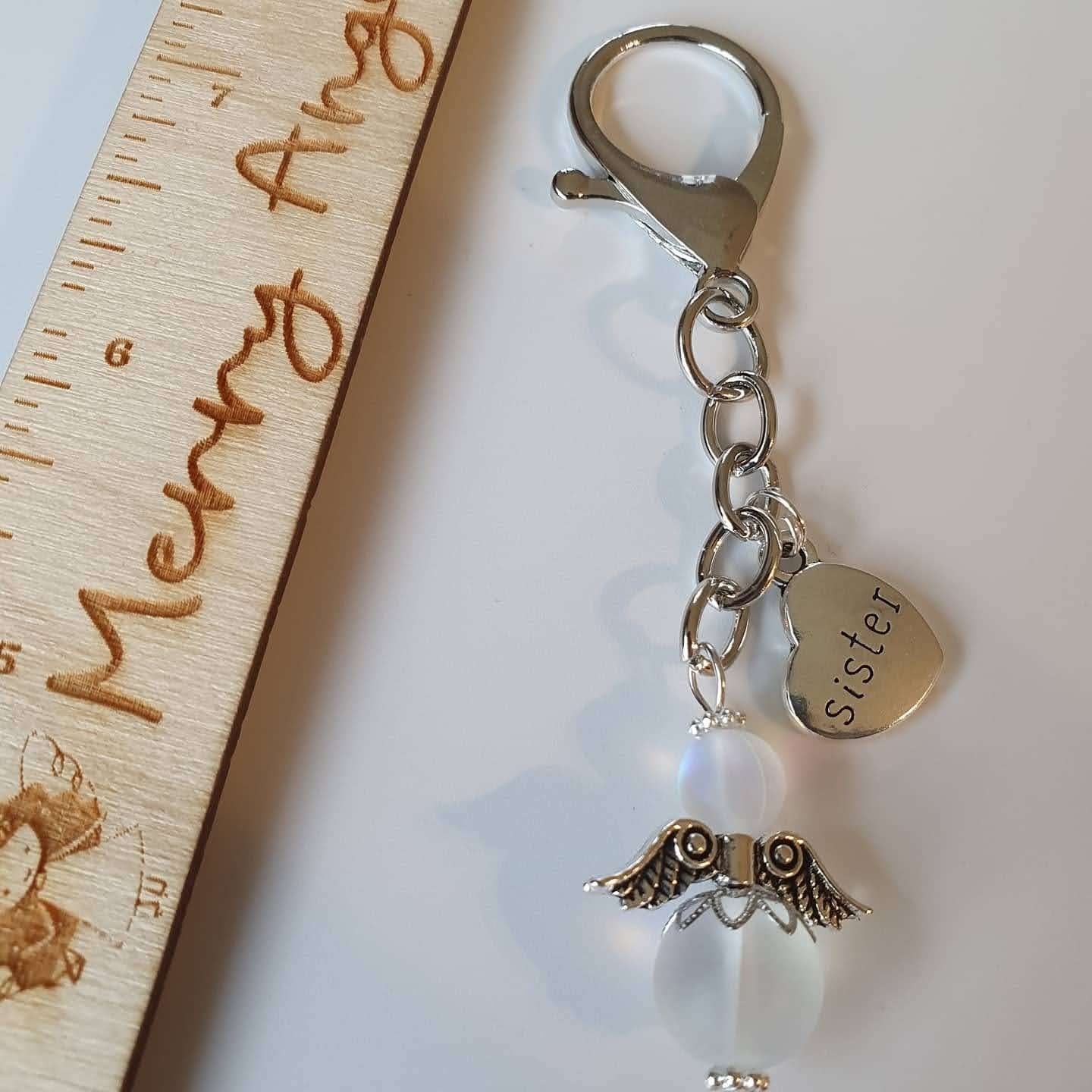 This is a picture of a silver angel keyring with a silver heart charm with the word 'sister' engraved on it