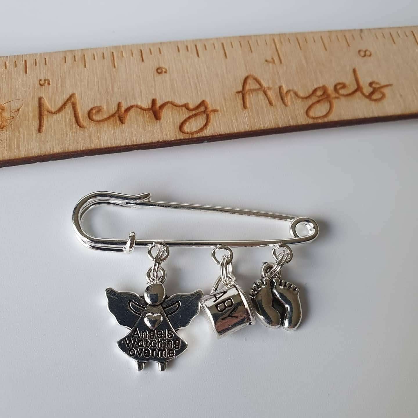 Picture is of a silver plated pram pin with baby feet, baby cup, and angel with the words Angels watching over me engraved on it