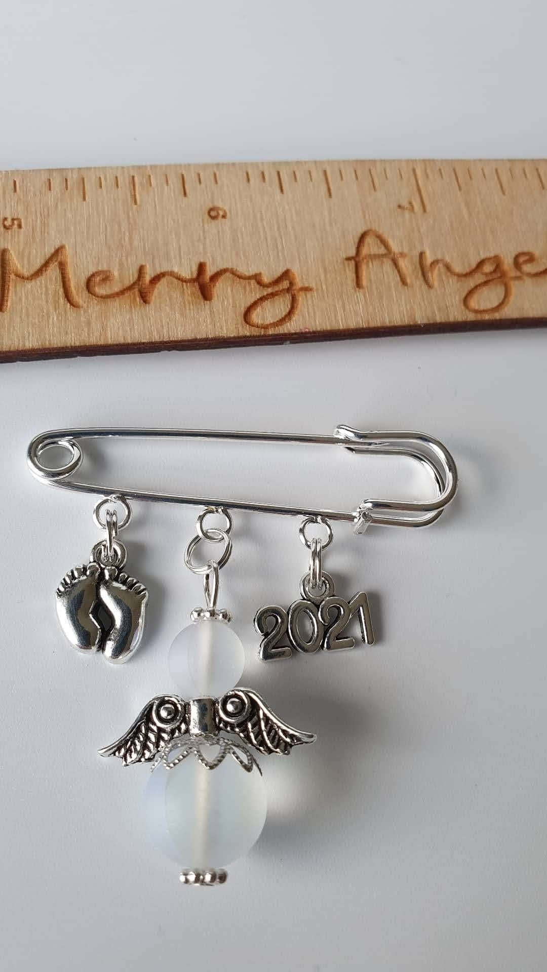 A silver plated pram pin with silver feet charm, a clear angel with silver wings and a silver 2021 charm.