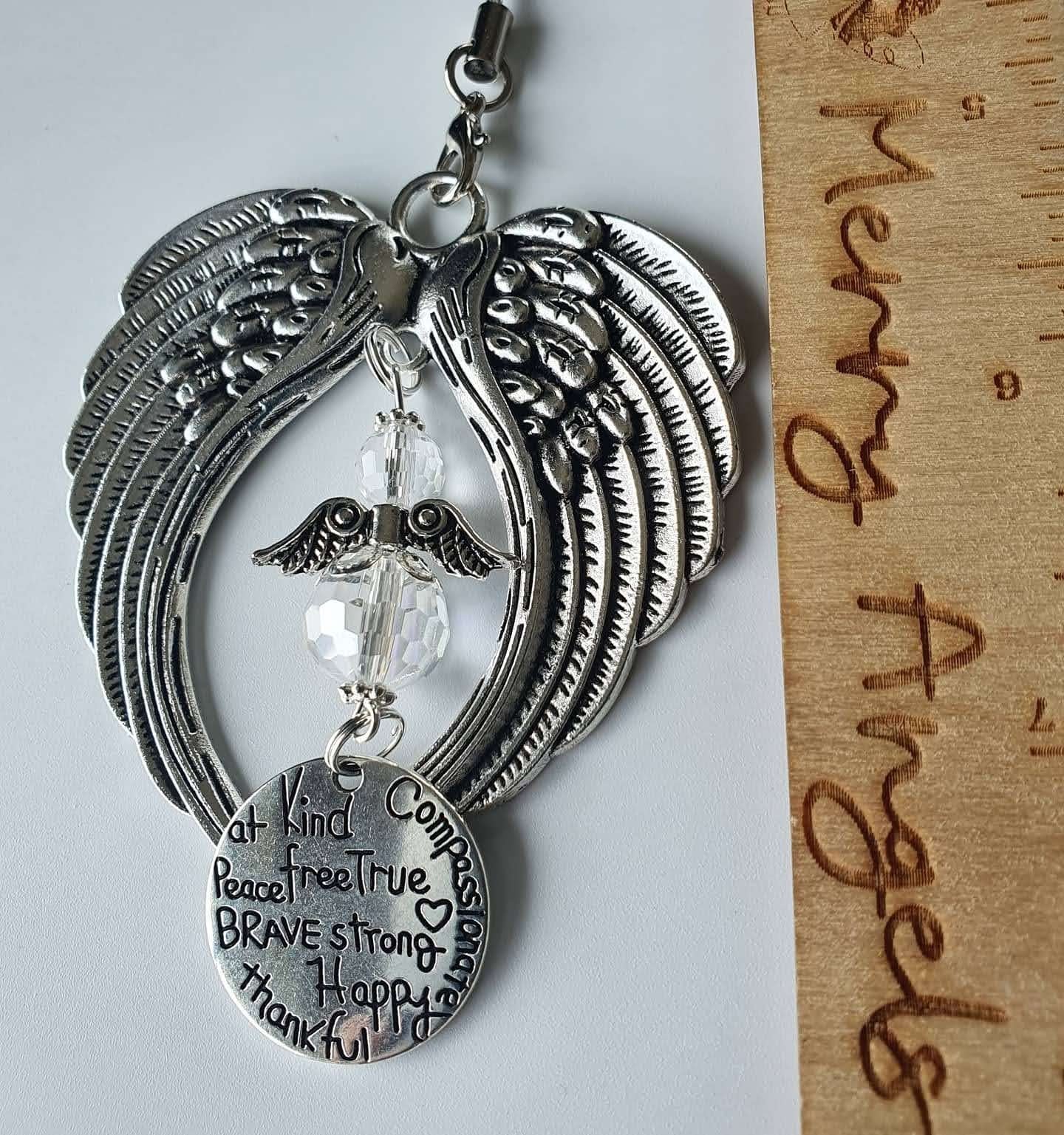 This is a picture of an angel wing hanging charm with a clear angel in the centre and a silver circle charm hanging from the angel. 