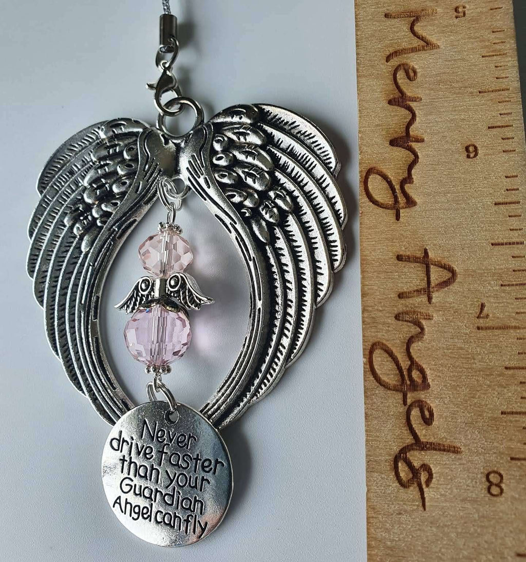 This is a picture of an angel wing hanging charm with a clear angel in the centre and a silver circle charm with the engraving ' Never drive faster than your guardian angel can fly'. 