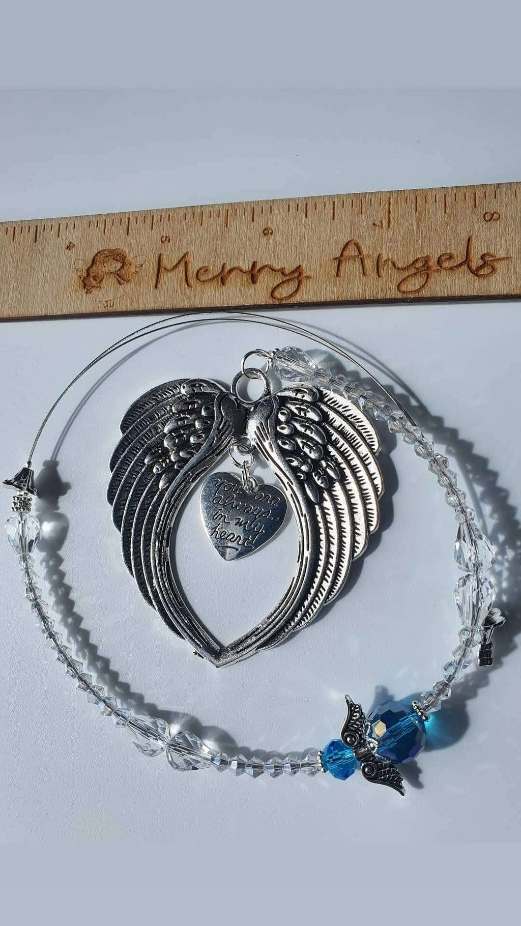 Silver angel wing hanging charm with silver heart charm in centre that reads: You are always in my heart. There is a blue angel with silver wings and clear beads too. 
