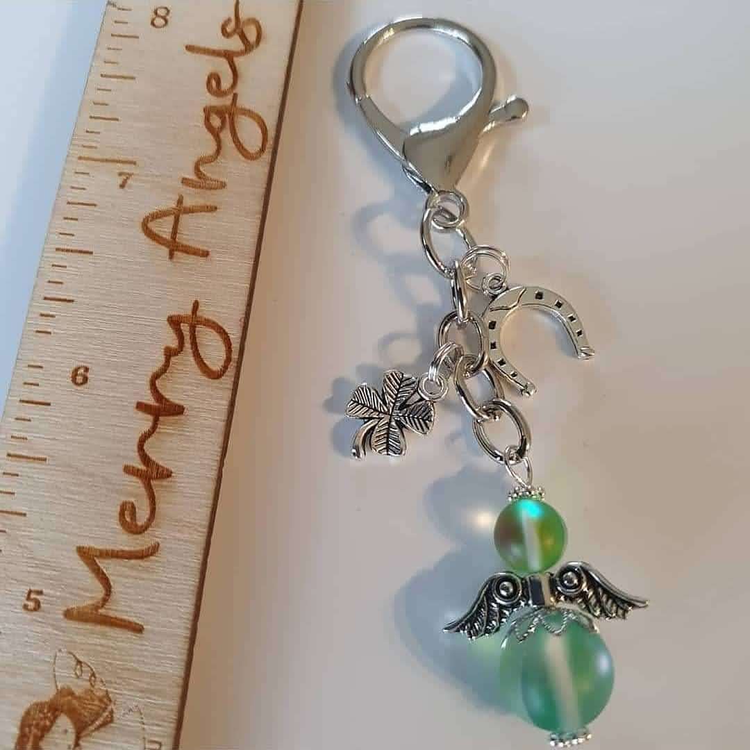 This is a picture of a silver angel keyring with two silver charms (a shamrock and a horseshoe). The angel is green. 