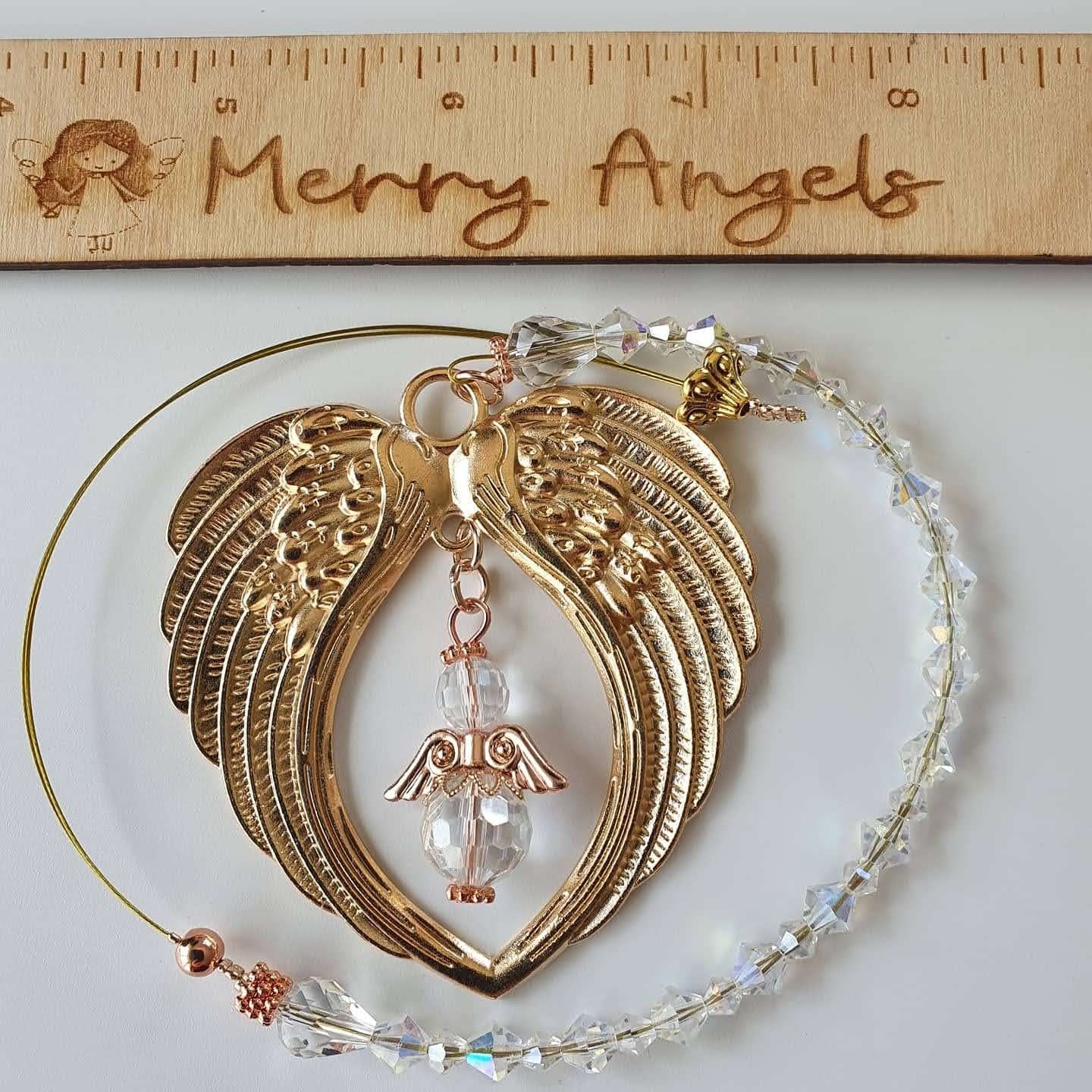 This is a picture of a rose gold angel wing hanging charm with a clear angel in the centre