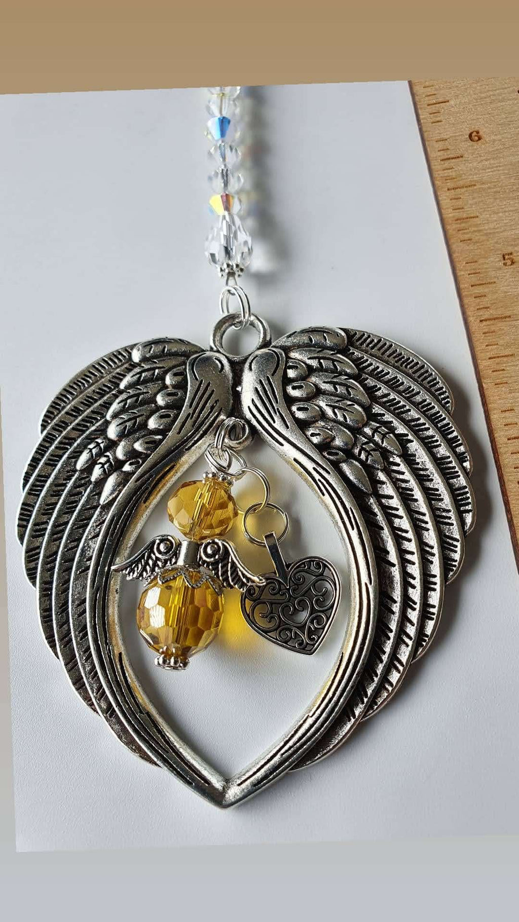 This is a picture of a silver angel wing hanging charm with a heart charm in the centre and a yellow angel with silver wings in the centre too.